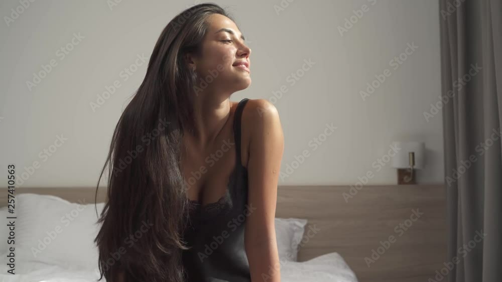 Beautiful girl in black silky nightie temptingly stretching and enjoying the rays of morning sun shining on her from the window. Beautiful girl in black silky nightie temptingly stretching and enjoying the rays of morning sun shining on her from the window.