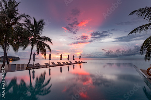 Beautiful poolside and sunset sky. Luxurious tropical beach landscape, deck chairs and loungers and water reflection © icemanphotos