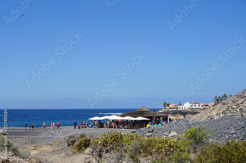 Beach bar from distance on the seacoast in La Caleta, Adeje, Tenerife, Canary Islands, Spain, seacoast, people © Anna