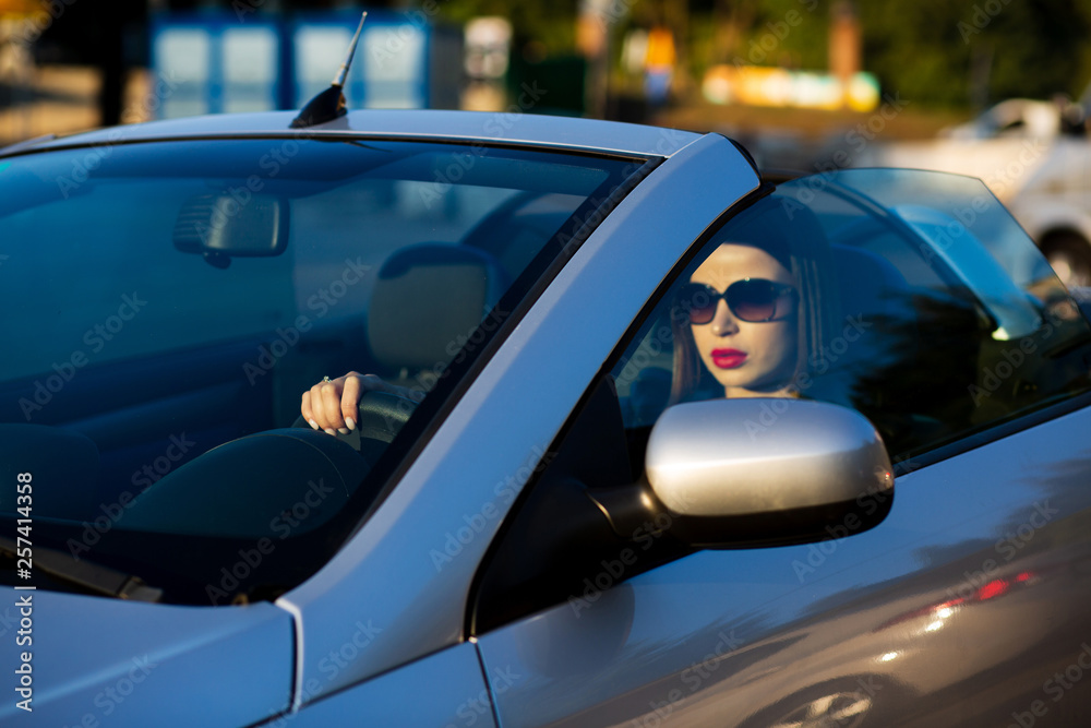 Closeup shot of attractive brunette girl with red lips wearing sunglasses driving a cabriolet. Empty space