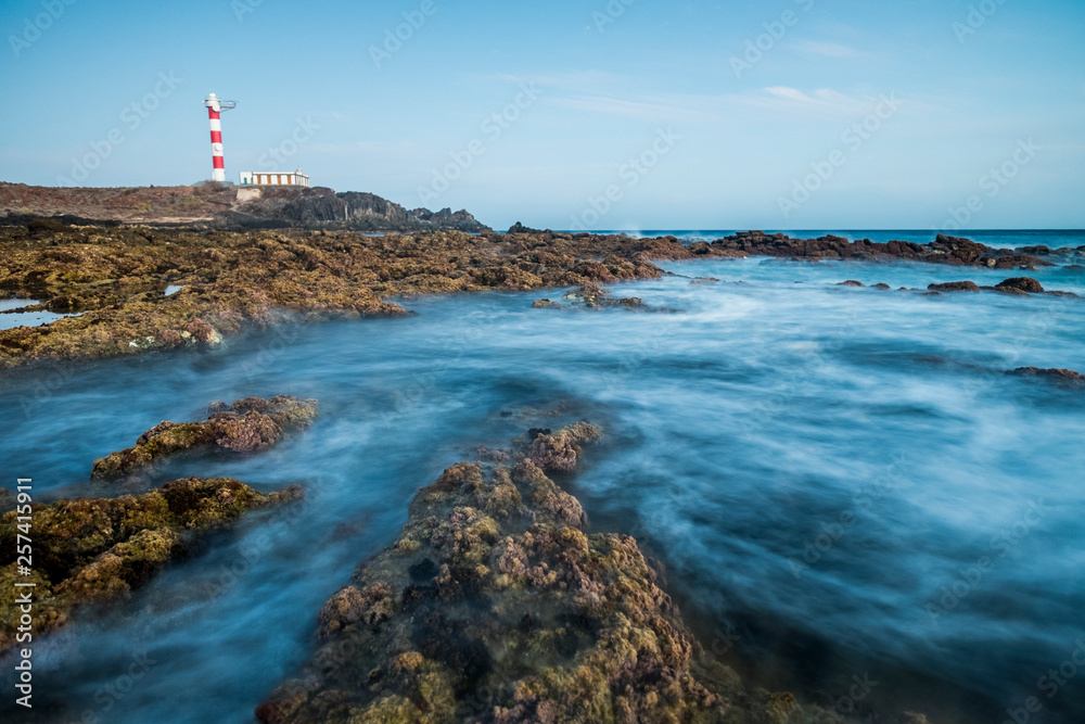 Long exposure water effect with rocks and beach and classic red white lighthouse in the background - travel and destination holiday concept - Blue tones and beautiful landscape