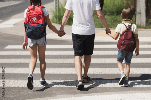 Fototapeta Responsible parent holding hands of children while walking through crosswalk