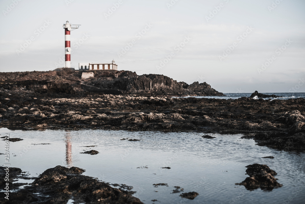 Long exposure water effect with rocks and beach and classic red white lighthouse in the background - travel and destination holiday concept