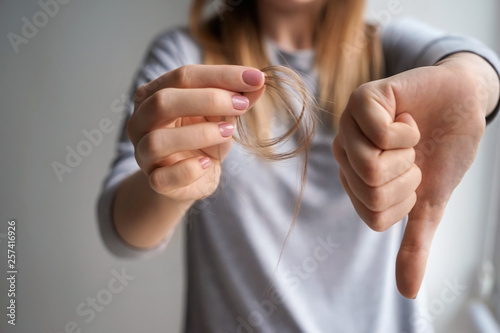 Woman with hair loss problem showing thumb-down on grey background