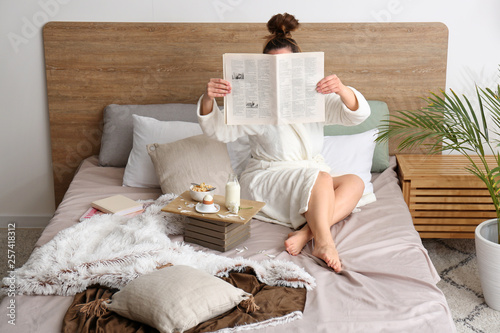 Young woman reading newspaper and having breakfast in bed