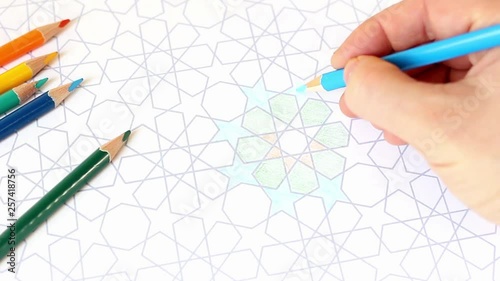 Closeup of human hand drawing, coloring decorative arab tile pattern with geometric stars. Composition with colored pencils on the table. Artistic concept. Ramadan HD footage.