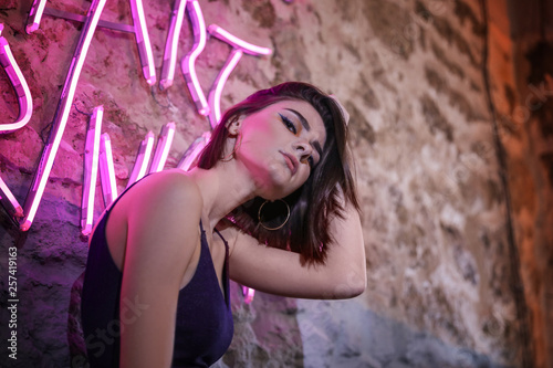 Portrait of beautiful young woman near neon lighting on wall