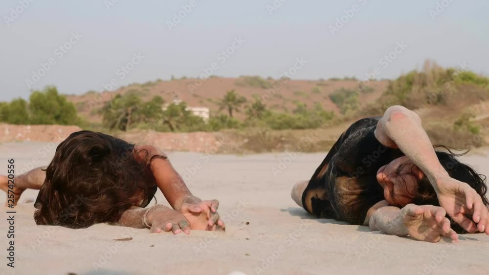 Mom and teenager daughter are doing relaxing exercise at the beach, rolling on the sand towards each other in slow motion. Family having fun,  front view.