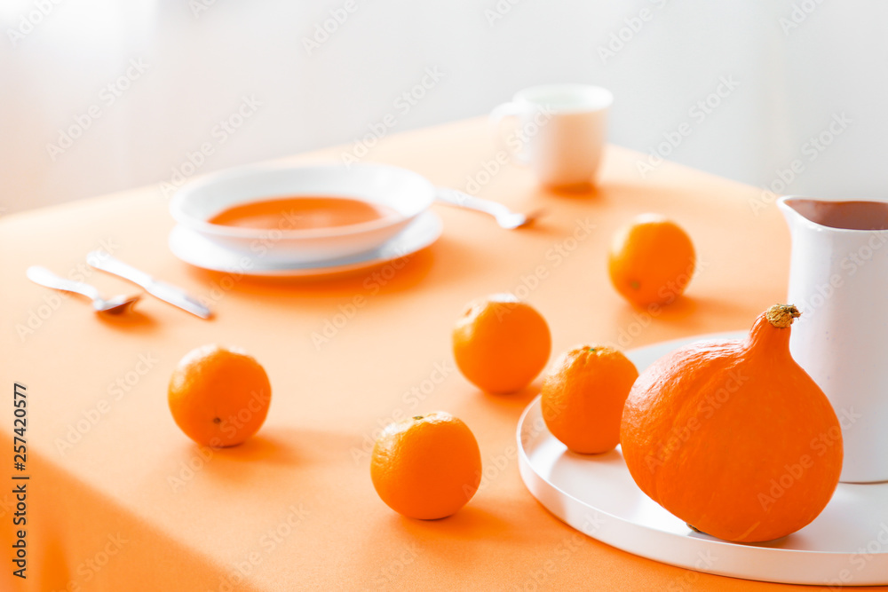 Real photo with close-up of dining table with cloth, fresh oranges, pumpkin and plate with soup in blurred background Real photo with close-up of dining table with cloth, fresh oranges, pumpkin and plate with soup in blurred background