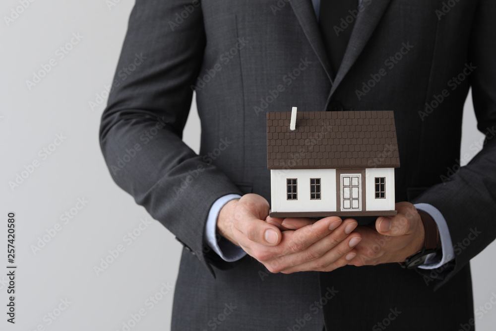 Insurance agent with model of house on light background, closeup. Protection of house from earthquake Insurance agent with model of house on light background, closeup. Protection of house from earthquake