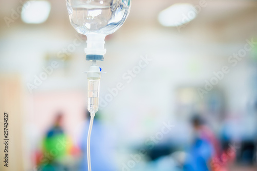 Close up saline IV drip for patient in hospital with copy space on n blurred doctor give medical and other attention to a sick person