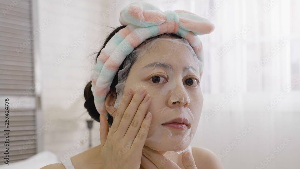 asian woman with cute headband on head hands put cosmetic mask on face. female looking camera as mirror applying facial moisturizer sheet relax in bedroom with white background. girl enjoy leisure. asian woman with cute headband on head hands put cosmetic mask on face. female looking camera as mirror applying facial moisturizer sheet relax in bedroom with white background. girl enjoy leisure.