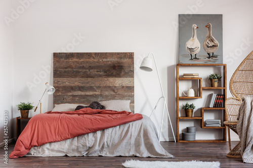 Comfortable king size bed with wooden rustic headboard and white industrial lamp next to it