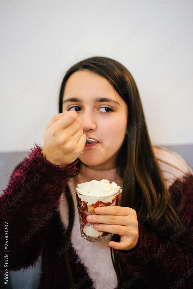 teen ager girl eating an ice cream with strawberries and cream - happy girl eating dessert - girl portraits teen ager girl eating an ice cream with strawberries and cream - happy girl eating dessert - girl portraits