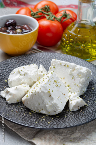 Fresh young soft white Feta cheese on black plate seasoned with dried oregano herb