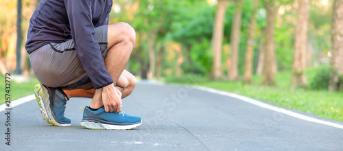 Young athlete man tying running shoes in the park outdoor, male runner ready for jogging on the road outside, asian Fitness walking and exercise on footpath in morning. wellness and sport concepts