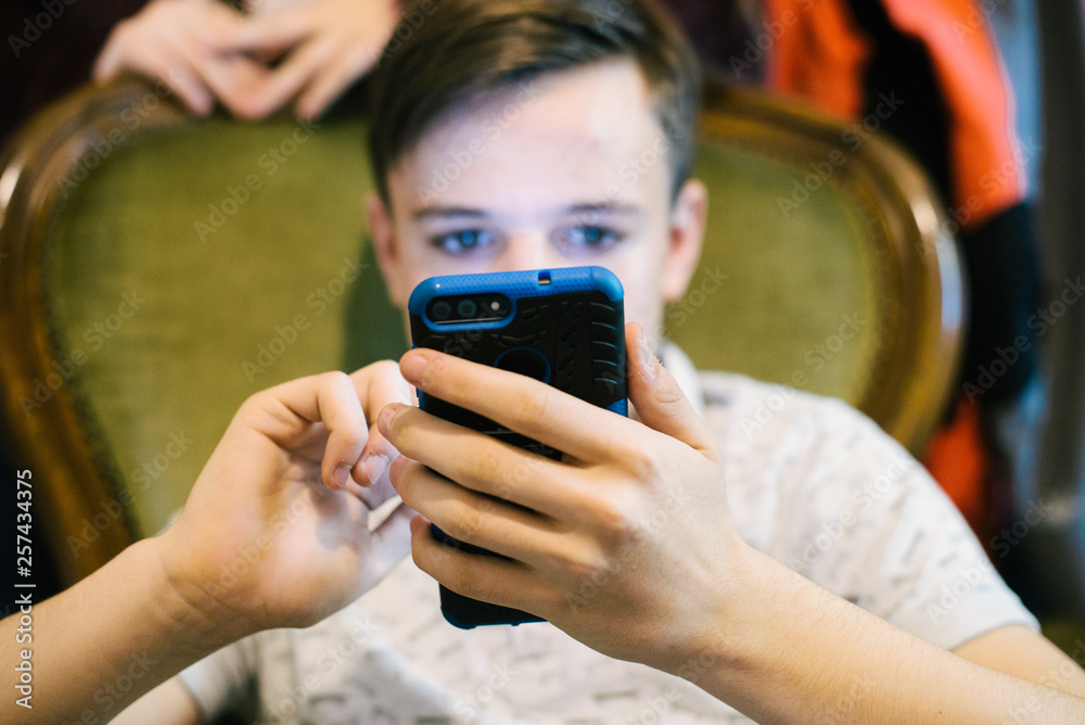 Fototapeta premium teen boy looks at the smartphone in his home- portrait of boy reading on the smartphone