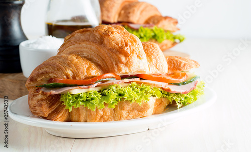 Fresh croissant or sandwich with salad, ham, jamon, prosciutto, salami, cheese, chicken, tomatoes on wooden background. Morning breakfast concept. Healthy and fast food. © jeny_lk