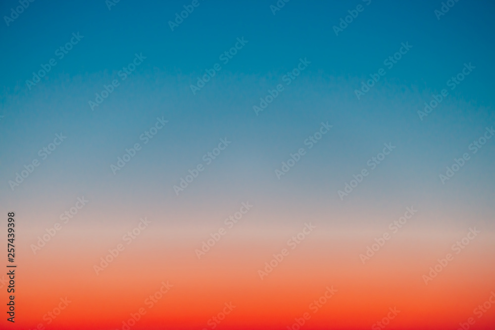 Obraz premium Predawn clear sky with red horizon and blue atmosphere. Smooth orange blue gradient of dawn sky. Background of beginning of day. Heaven at early morning with copy space. Sunset, sunrise backdrop.