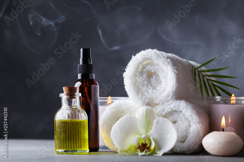 Aromatherapy, spa, beauty treatment and wellness background with massage oil, orchid flowers, towels, cosmetic products and burning candles.