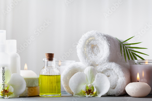 Spa, beauty treatment and wellness background with massage oil, orchid flowers, towels, cosmetic products and burning candles.