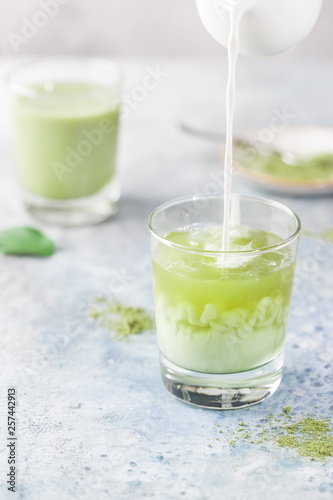 Iced Matcha green latte in glasses with matcha powder on light background.