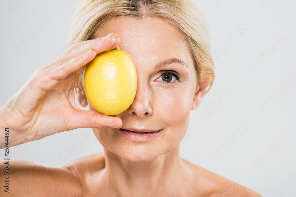 beautiful and mature woman holding ripe lemon and looking at camera isolated on grey beautiful and mature woman holding ripe lemon and looking at camera isolated on grey