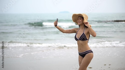 Wallpaper Mural beautiful young asian woman in black bikini and sun hat walking on the sea beach take a picture of herself .summer vacations .girl in  swimsuit  takes selfie photo. Torontodigital.ca