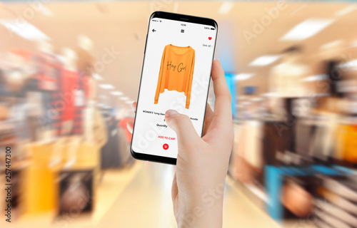 Female hand in clothing store buying yellow hoodie online on her smartphone
