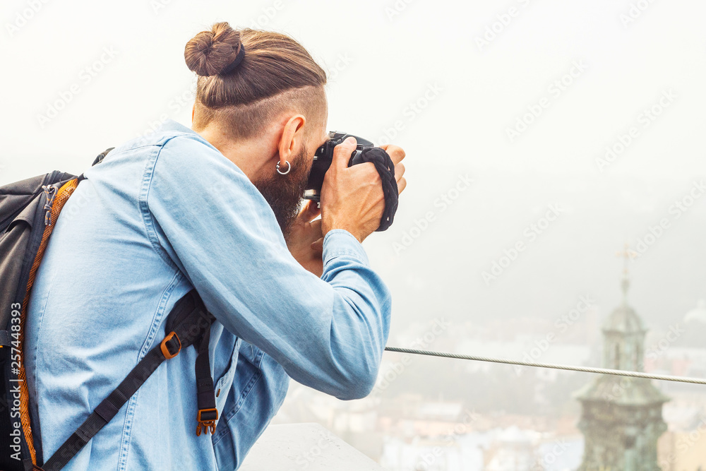 Obraz premium Traveler Young Man with a Beard Photographs Attractions and Panorama of the Ancient City from a High Observation Platform. Travel Tourism Concept