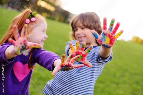 two young cheerful children show their hands stained with colorful paints