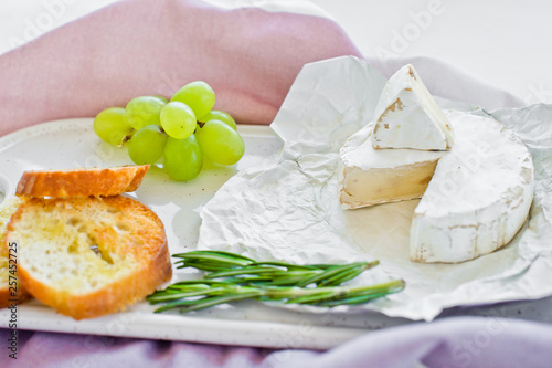 Brie cheese with nuts on a white cutting Board, grapes, rosemary. White background, side view