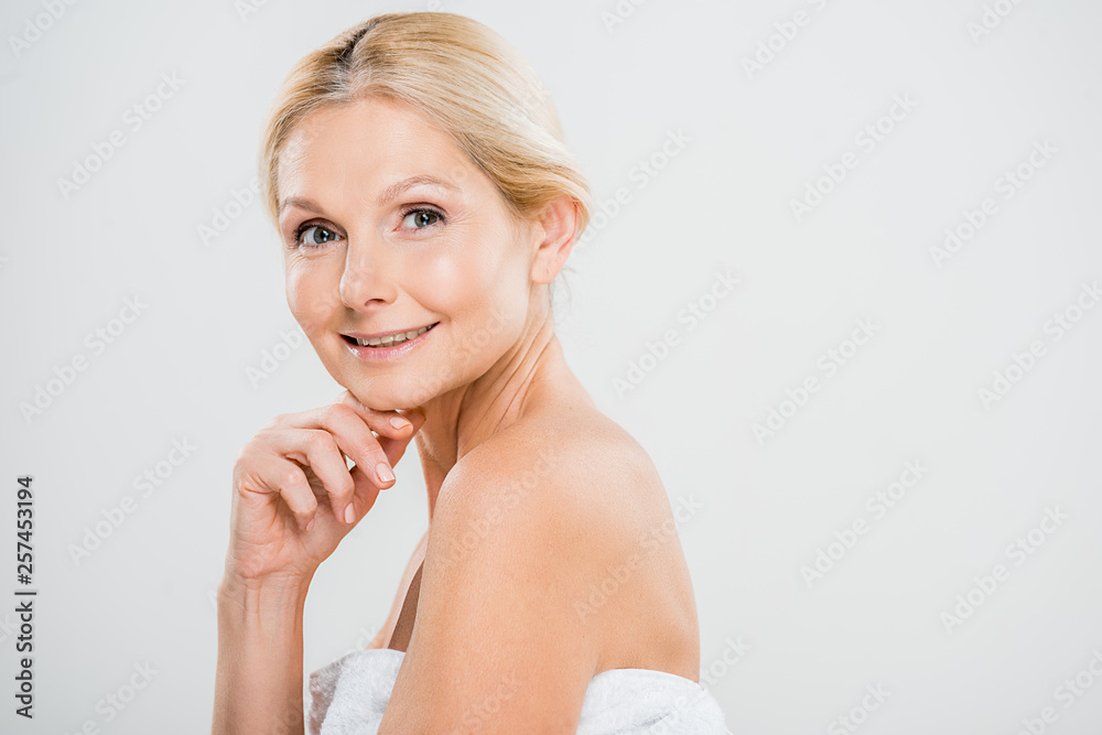 attractive and smiling mature woman looking at camera and touching her face on grey background attractive and smiling mature woman looking at camera and touching her face on grey background
