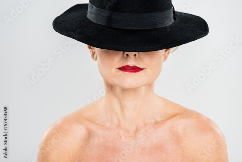 middle aged elegant and fashionable woman with red lips in black hat isolated on grey © LIGHTFIELD STUDIOS