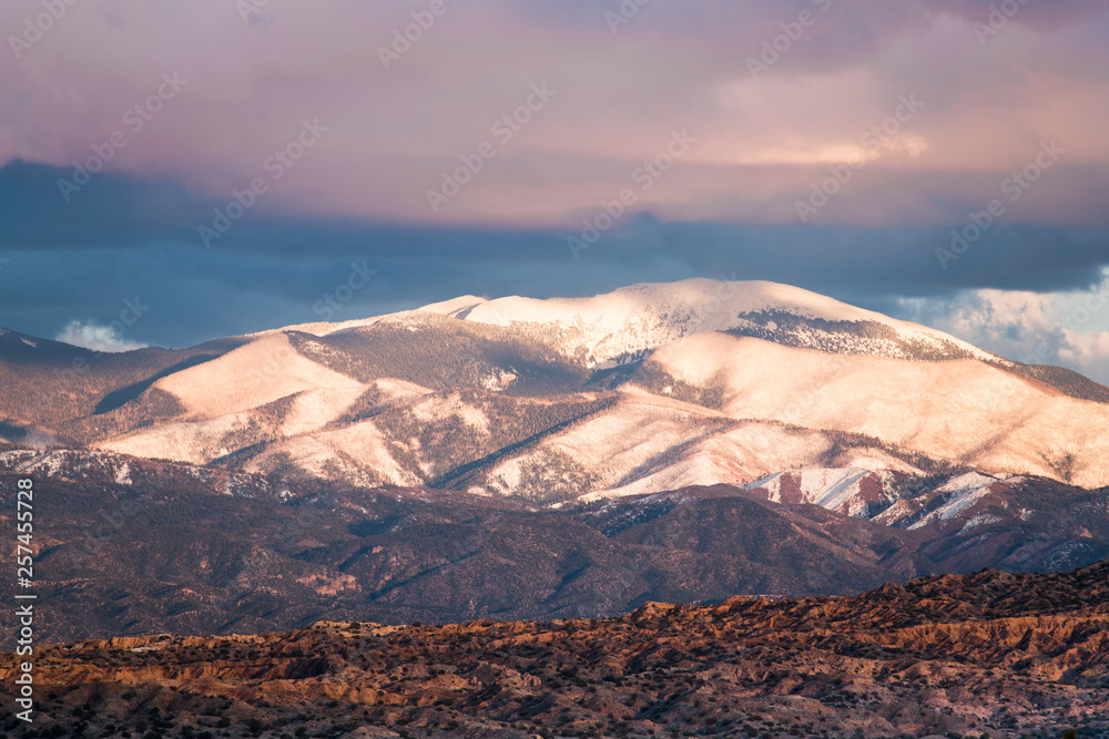 Obraz premium Zachód słońca oświetla ośnieżone góry Sangre de Cristo oraz kolorowe chmury i badlands w pobliżu Santa Fe w Nowym Meksyku