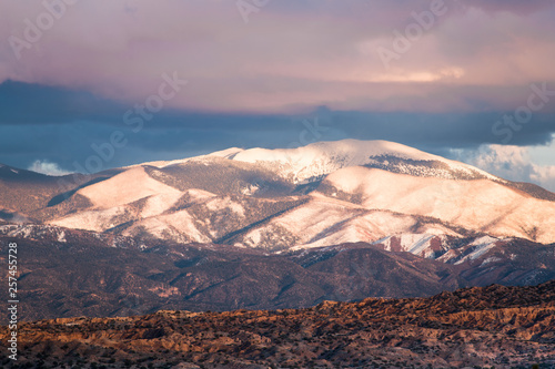 Sunset illuminates the snow-capped Sangre de Cristo Mountains and colorful clouds and badlands near Santa Fe, New Mexico