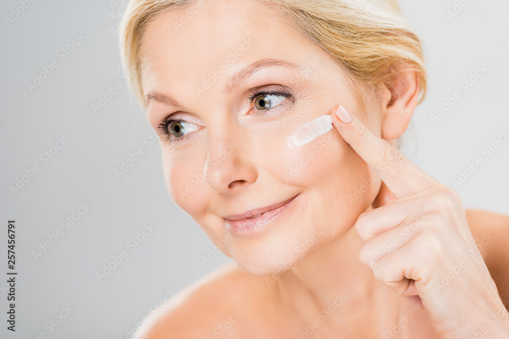 beautiful and mature woman looking away and applying cosmetic cream on face beautiful and mature woman looking away and applying cosmetic cream on face