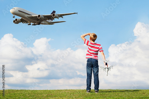 Boy holding model plane while passenger plane flies overhead
