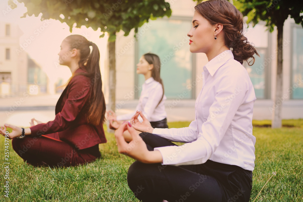 Three young girls dressed in office clothes are practicing yoga on the grass Three young girls dressed in office clothes are practicing yoga on the grass