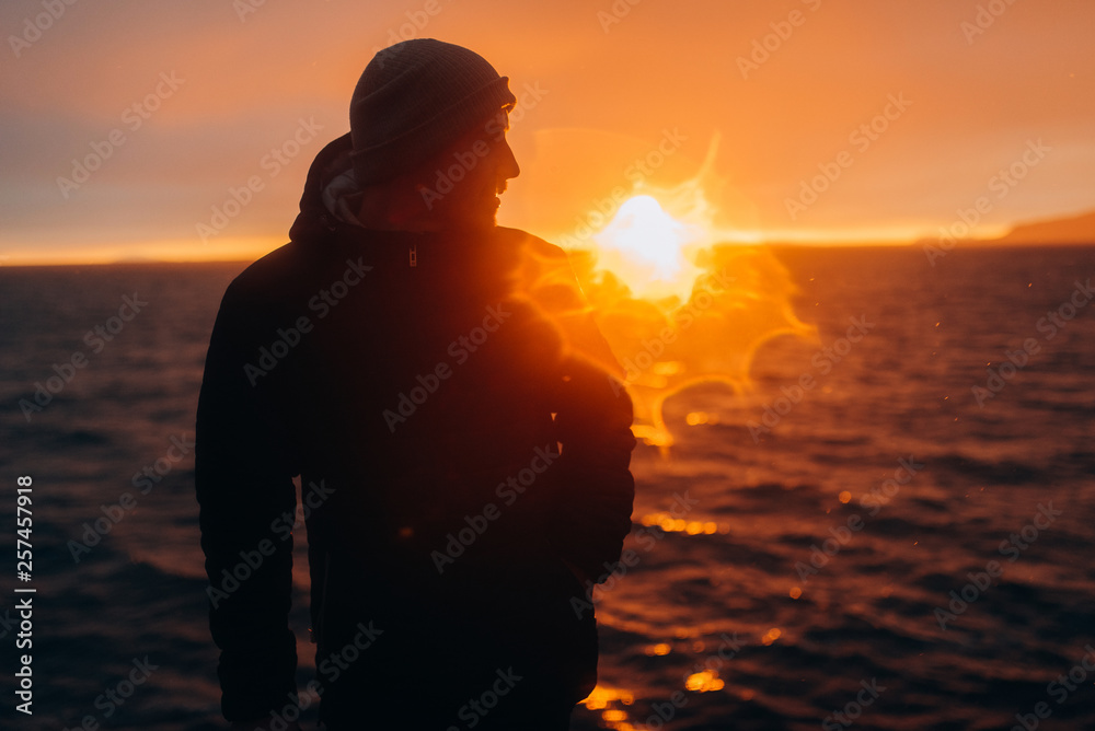 Silhouette of the guy in the sunset. The guy stands at the sunset by the sea.