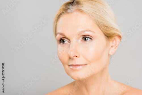attractive and blonde mature woman looking away isolated on grey