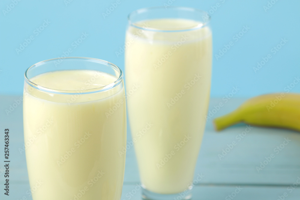 A glass with a banana milkshake and a fresh banana on a blue background. Making a milkshake.