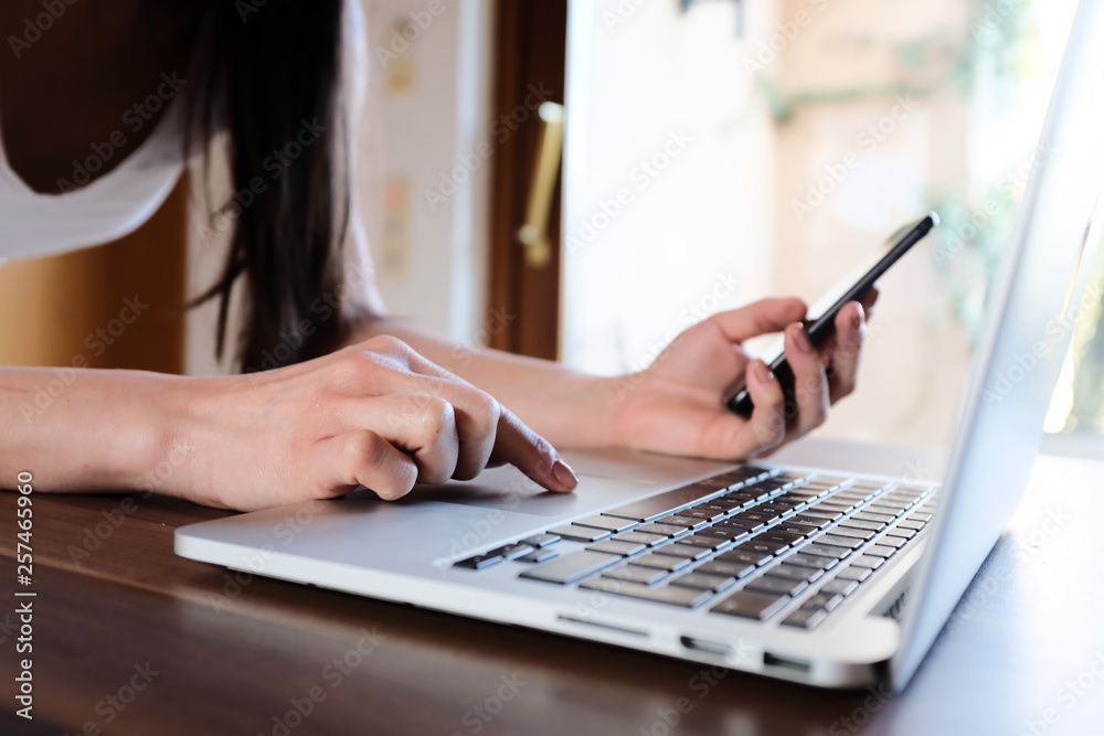 Frau hält Handy in der Hand und arbeitet am Laptop Frau hält Handy in der Hand und arbeitet am Laptop