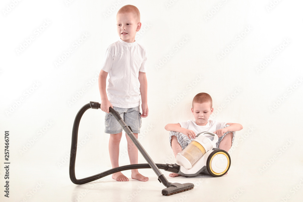 Two happy children in home's clothers, pretty blond boys is going to clean the dust in the room. Compact vacuum cleaner. The concept of cleanliness and hygiene. Two happy children in home's clothers, pretty blond boys is going to clean the dust in the room. Compact vacuum cleaner. The concept of cleanliness and hygiene.