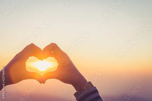 Hands forming a heart shape with sunrise silhouette,copy space,warm retro tone.