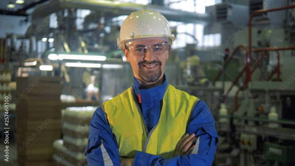 Factory worker in a hardhat is smiling at the camera Factory worker in a hardhat is smiling at the camera