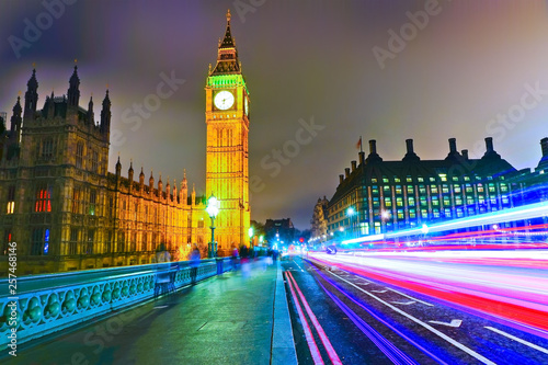 Houses of Parliament from Westminster Bridge with lots of cars passing through in London at night.