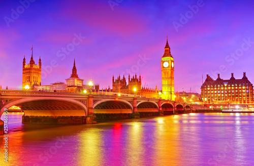 View of the Houses of Parliament and Westminster Bridge along River Thames in London at dusk.