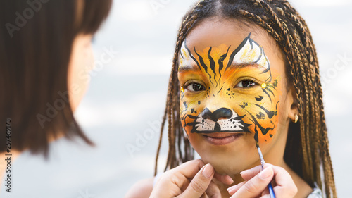 Little girl getting her face painted by face painting artist. photo