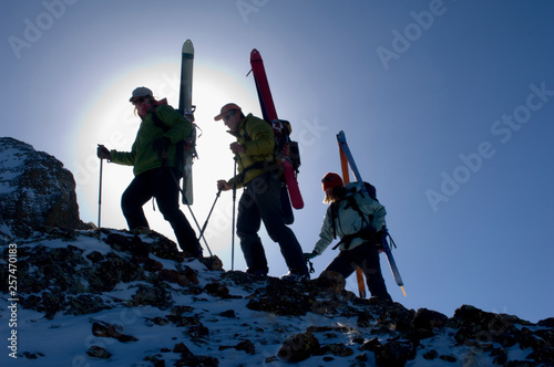 Silhouette of three skiers, Rob Fullerton, Joe Ryan, Janet Smith, with ski equipment attached to their backpacks climbing up a rocky slope with a sun burst halo around them in the San Juan Mountains, Uncomphagre National Forest, Colorado. photo